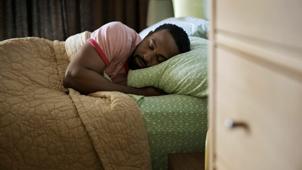 man sleeping under blanket on bed