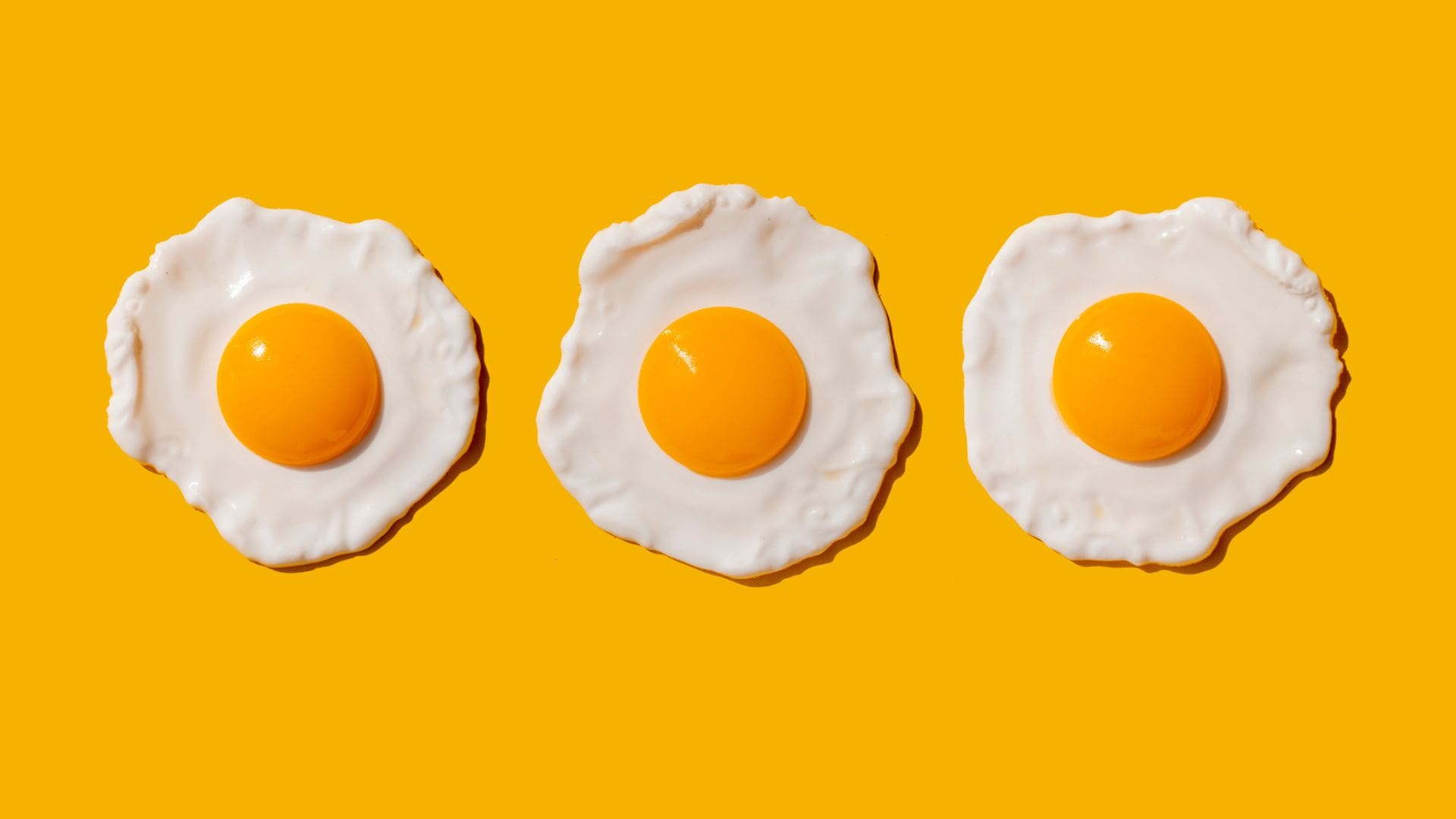 three fried eggs on yellow backdrop to illustrate benefits of eggs against alzheimers
