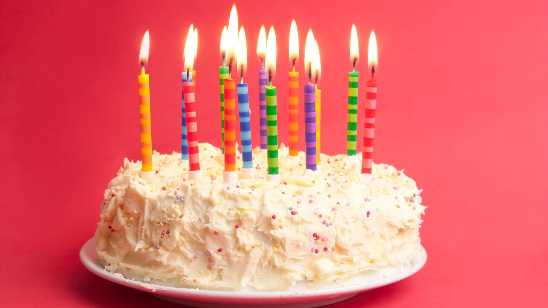 birthday cake with white frosting decked with lit candles against pink backdrop